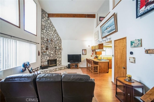 living area with beam ceiling, a fireplace, a towering ceiling, and wood finished floors