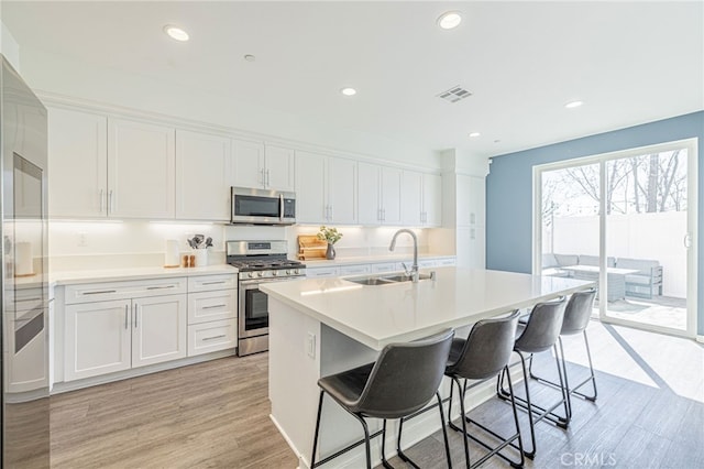 kitchen featuring visible vents, a breakfast bar area, appliances with stainless steel finishes, white cabinets, and a sink