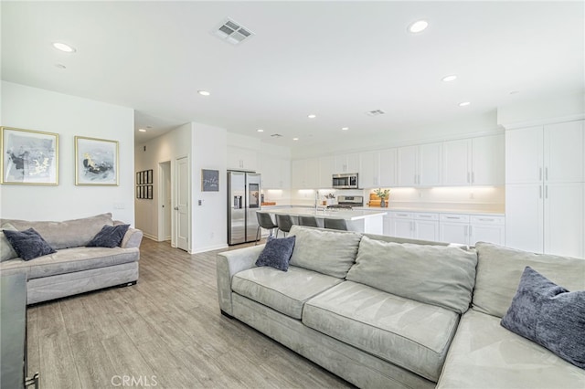 living room with visible vents, recessed lighting, light wood-type flooring, and baseboards