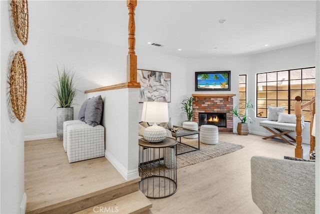 living area with recessed lighting, visible vents, a brick fireplace, wood finished floors, and baseboards