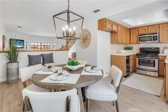 dining room with light wood-style flooring, a notable chandelier, recessed lighting, visible vents, and a tray ceiling