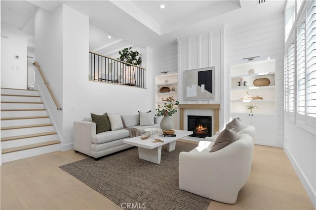 living area with wood finished floors, a tray ceiling, recessed lighting, stairs, and a glass covered fireplace