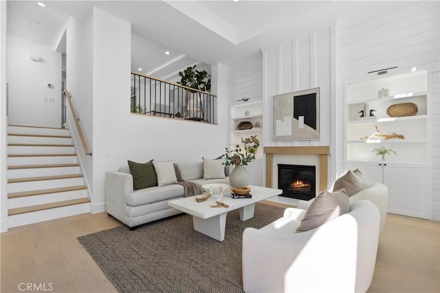 living room with built in features, stairs, recessed lighting, wood finished floors, and a glass covered fireplace