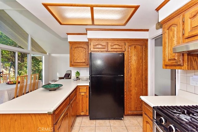 kitchen featuring a peninsula, light tile patterned flooring, freestanding refrigerator, light countertops, and brown cabinets