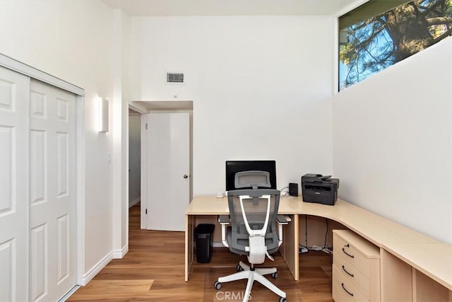 home office featuring visible vents, a towering ceiling, and light wood finished floors