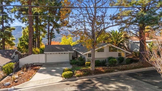 mid-century home with fence, a garage, driveway, and stucco siding