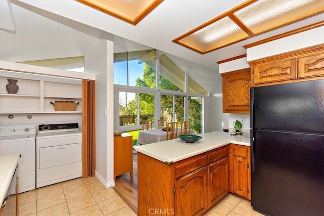 kitchen featuring light tile patterned floors, lofted ceiling, a peninsula, freestanding refrigerator, and light countertops