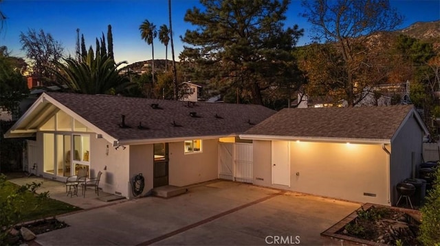 rear view of house with stucco siding, a patio, and roof with shingles