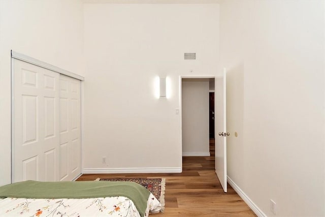 bedroom with visible vents, wood finished floors, a closet, a high ceiling, and baseboards