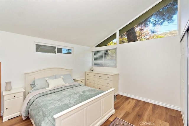 bedroom with vaulted ceiling, light wood-style floors, and baseboards