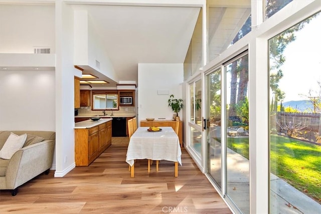 dining space with light wood finished floors, visible vents, high vaulted ceiling, and baseboards