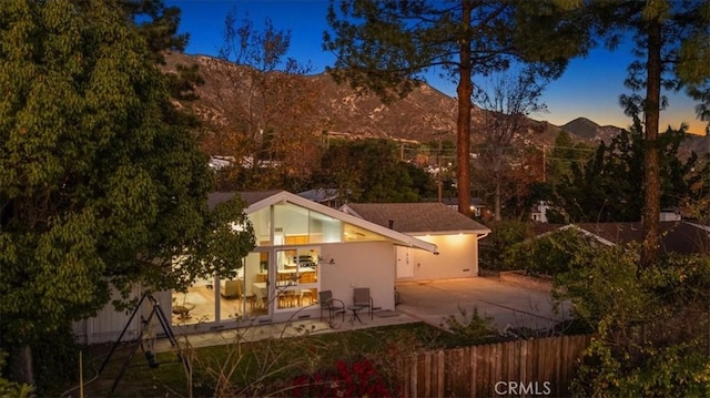 back of house at dusk with a patio area, a mountain view, and fence