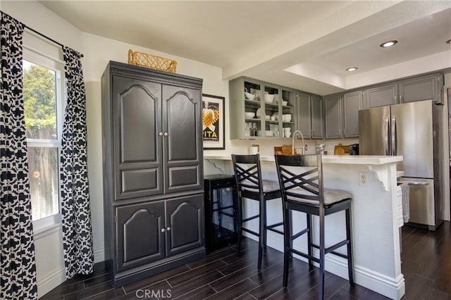 kitchen featuring light countertops, freestanding refrigerator, wood tiled floor, a peninsula, and a kitchen breakfast bar