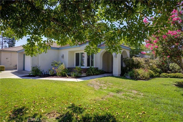 mediterranean / spanish house featuring an attached garage, driveway, a front lawn, and stucco siding