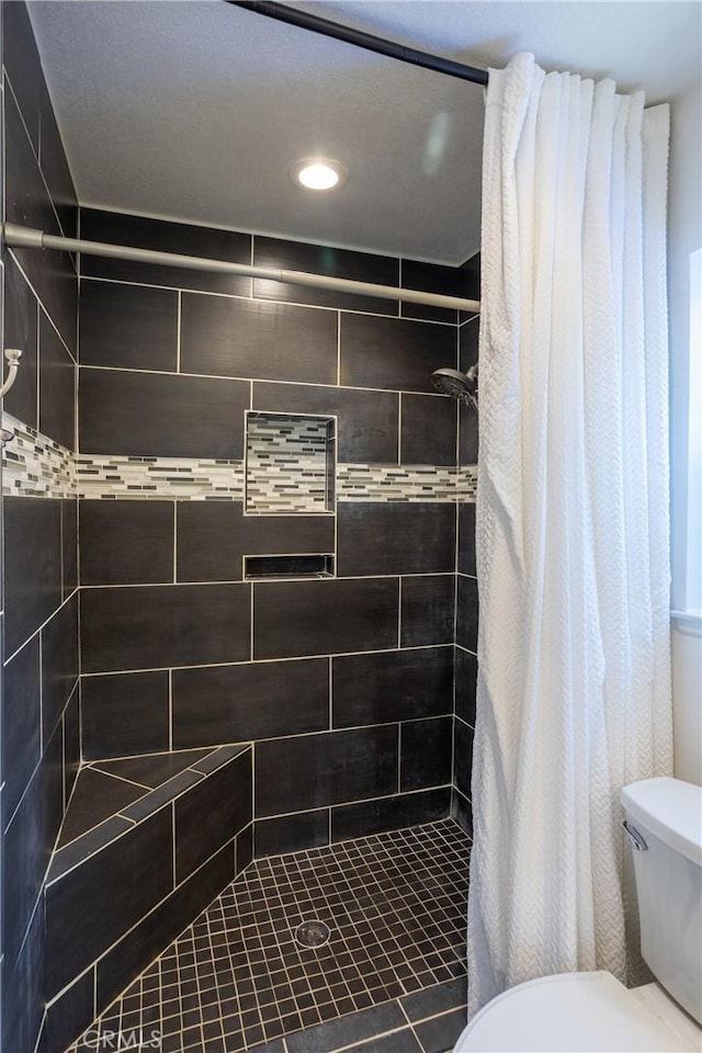 bathroom featuring tiled shower and toilet