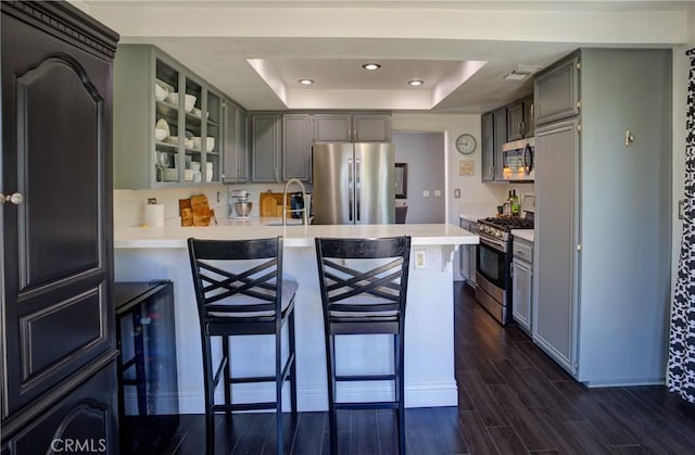 kitchen featuring a breakfast bar, a raised ceiling, appliances with stainless steel finishes, wood tiled floor, and a peninsula