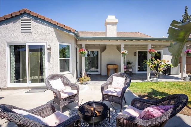 rear view of property featuring an outdoor living space with a fire pit, a patio area, a chimney, and stucco siding