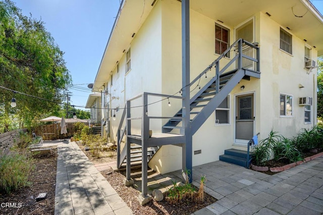 property entrance with stucco siding, a wall mounted AC, crawl space, a patio area, and fence