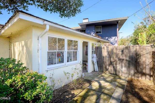 view of home's exterior with a chimney, fence, a patio, and stucco siding