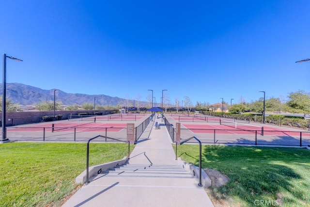 view of tennis court featuring a mountain view, a yard, and fence