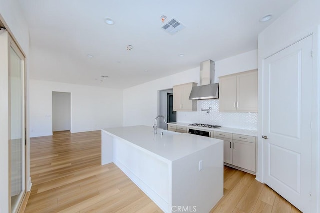 kitchen featuring light wood-type flooring, wall chimney range hood, visible vents, and gas cooktop