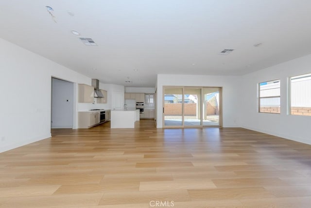 unfurnished living room featuring light wood-style floors, visible vents, a sink, and baseboards