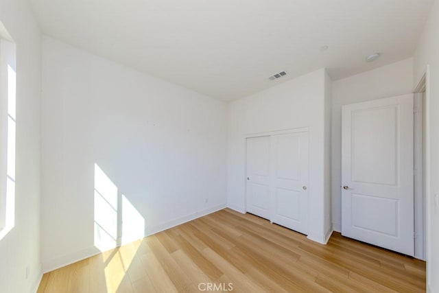 unfurnished bedroom featuring light wood-type flooring, baseboards, visible vents, and a closet