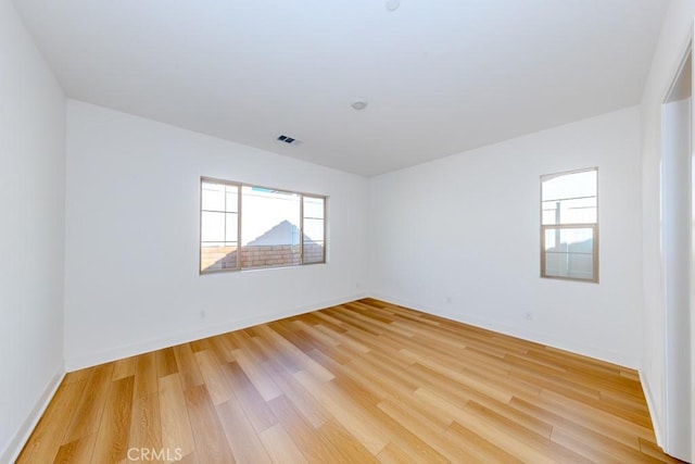 empty room with light wood finished floors, baseboards, and visible vents