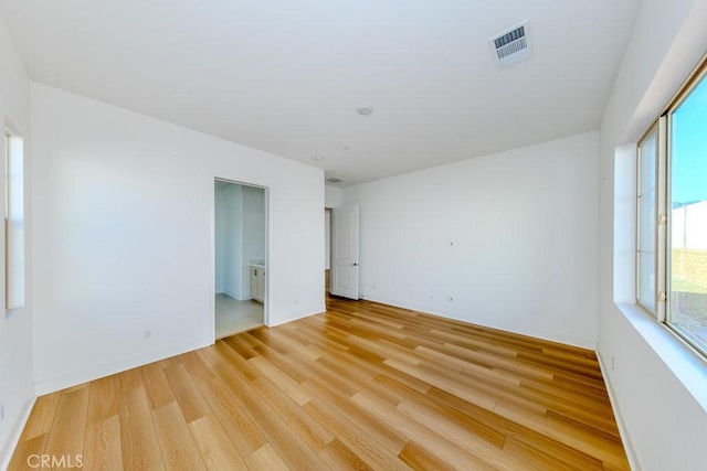 empty room with light wood-type flooring, visible vents, and baseboards