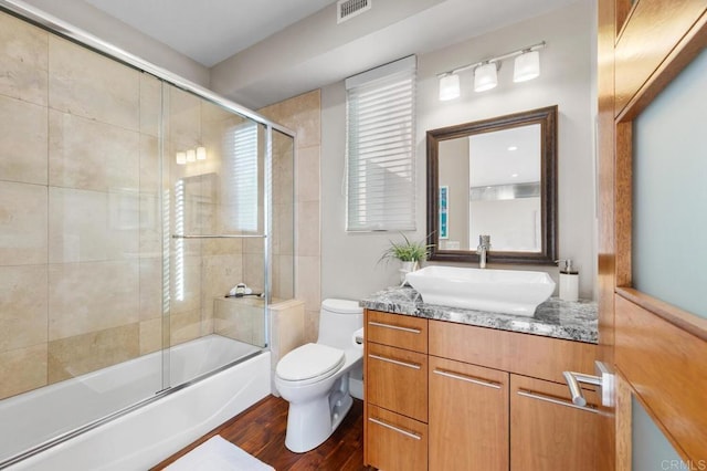 bathroom with vanity, visible vents, wood finished floors, toilet, and enclosed tub / shower combo