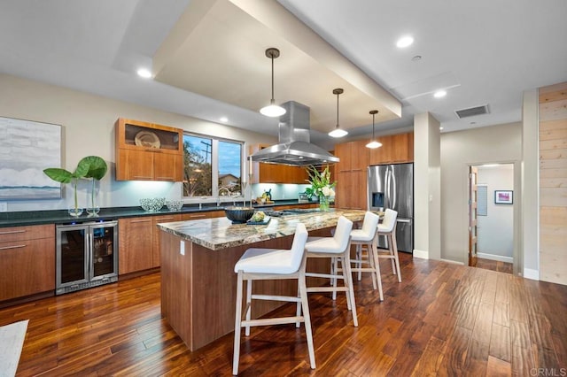 kitchen featuring brown cabinets, beverage cooler, stainless steel appliances, island range hood, and visible vents