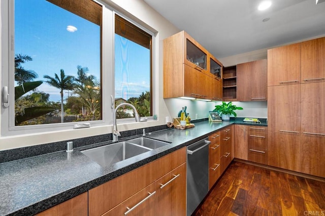 kitchen featuring stainless steel dishwasher, open shelves, brown cabinetry, dark stone counters, and a sink