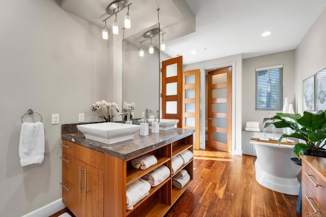 bathroom with a sink, a freestanding tub, double vanity, and wood finished floors