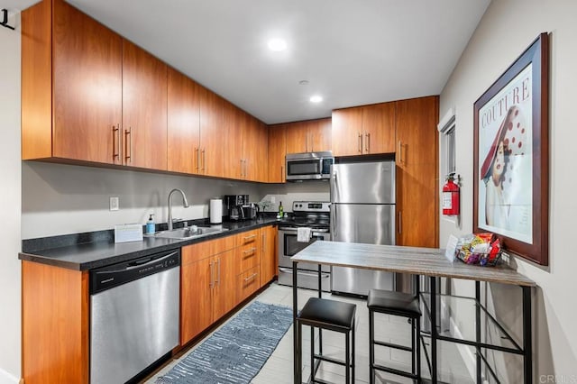 kitchen featuring a sink, appliances with stainless steel finishes, brown cabinetry, and dark countertops