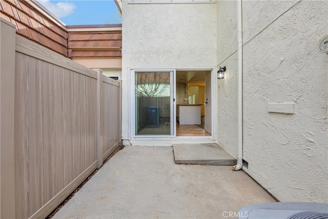 entrance to property featuring fence, a patio, and stucco siding