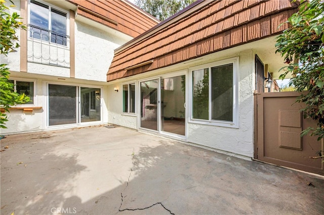 back of property with a tiled roof, mansard roof, a patio, and stucco siding