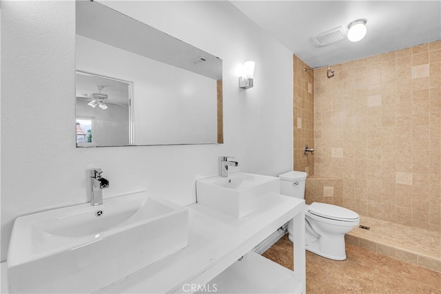 full bath with a tile shower, toilet, a sink, and visible vents