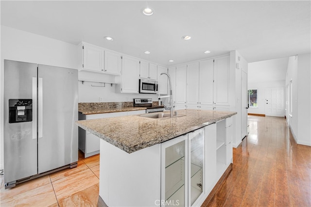 kitchen featuring light stone counters, light wood-style flooring, appliances with stainless steel finishes, white cabinets, and an island with sink