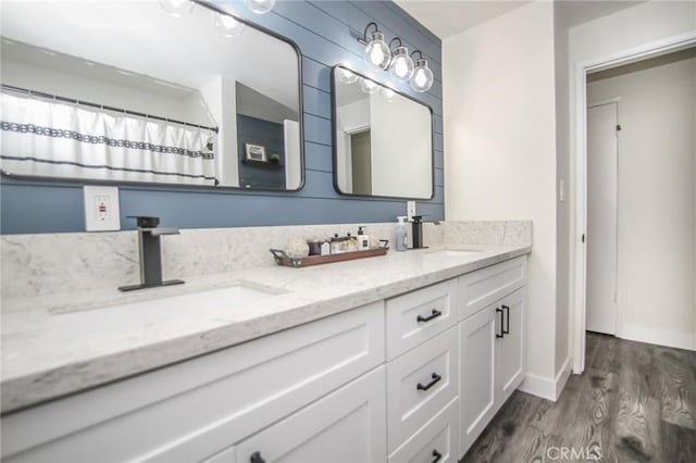 bathroom with double vanity, baseboards, a sink, and wood finished floors