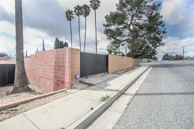 view of street featuring curbs, traffic signs, sidewalks, and a gate