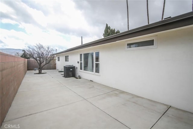 view of side of property featuring a patio, a fenced backyard, cooling unit, and stucco siding