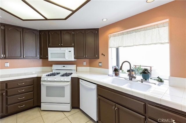 kitchen featuring dark brown cabinetry, white appliances, tile countertops, and a sink