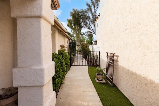 view of side of property featuring a gate, fence, and stucco siding