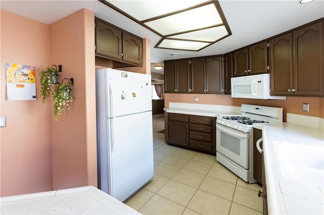 kitchen with light tile patterned floors, white appliances, tile counters, and dark brown cabinetry