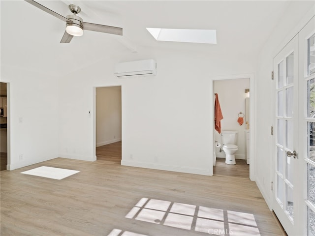 unfurnished room with vaulted ceiling with skylight, a wall unit AC, a ceiling fan, and light wood-style floors