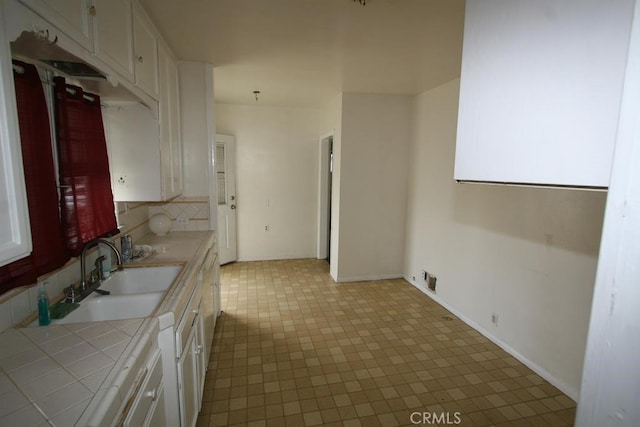 kitchen featuring tile countertops, a sink, baseboards, white cabinets, and decorative backsplash