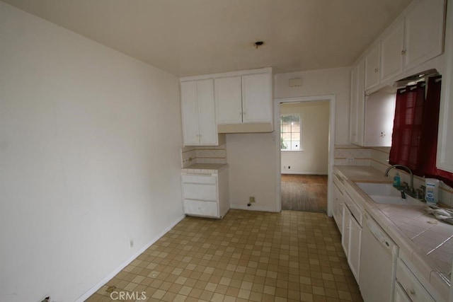 kitchen with tile counters, baseboards, dishwasher, white cabinetry, and a sink