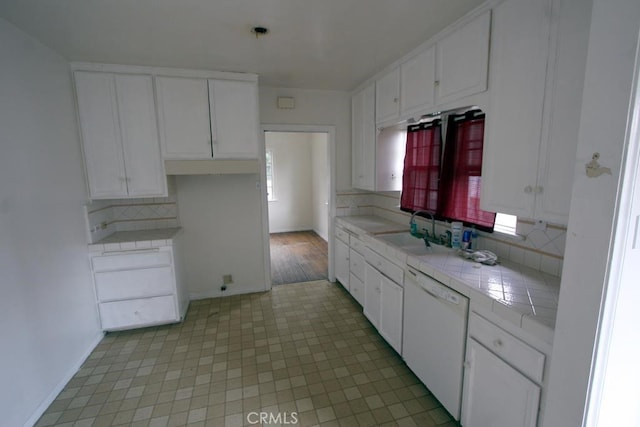 kitchen with tile countertops, white dishwasher, a sink, and white cabinets