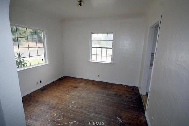 empty room featuring plenty of natural light, wood-type flooring, and baseboards