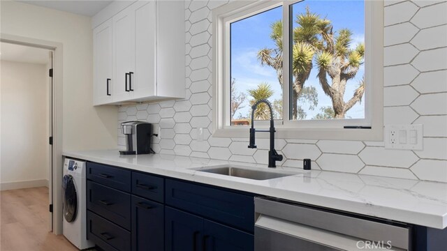 kitchen with washer / dryer, a sink, dishwasher, blue cabinets, and backsplash